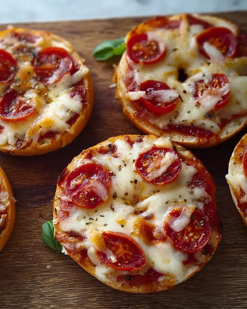Easy Mini Bagel Pizzas 3 Mini bagel pizzas baking in an oven.